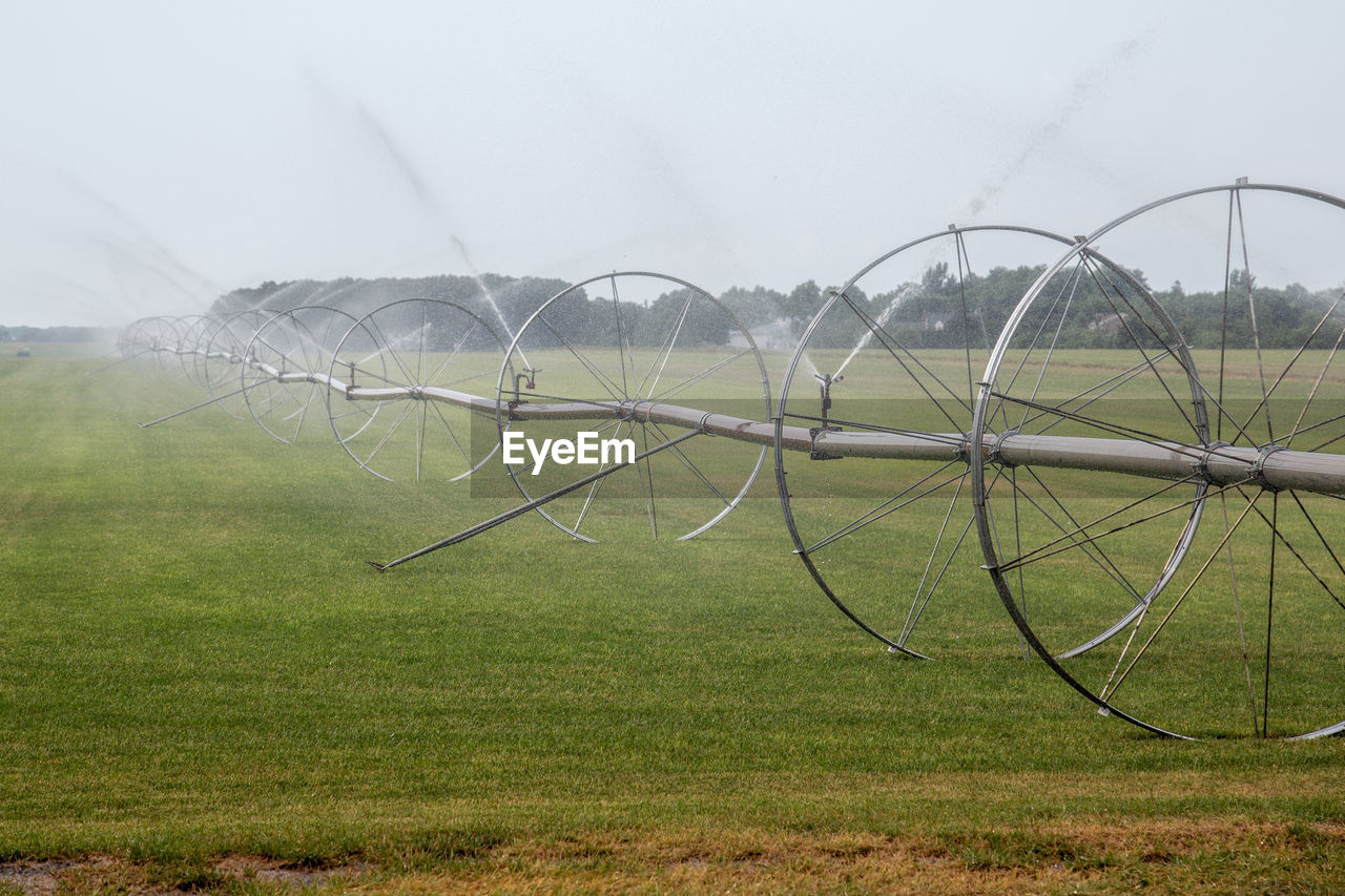 Agricultural sprinkler spraying on grassy field at farm against sky