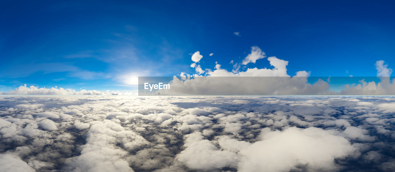 sky, cloud, blue, environment, nature, cloudscape, aerial view, horizon, landscape, beauty in nature, scenics - nature, flying, airplane, no people, travel, sunlight, outdoors, atmosphere, mountain range, white, air vehicle, high up, day, transportation, fluffy, idyllic, mountain, sun, space, dramatic sky, backgrounds, copy space