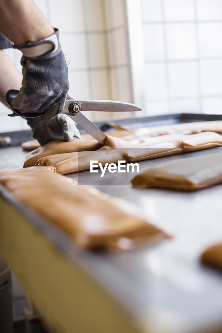 Cropped image of worker cutting caramel with scissors in candy store