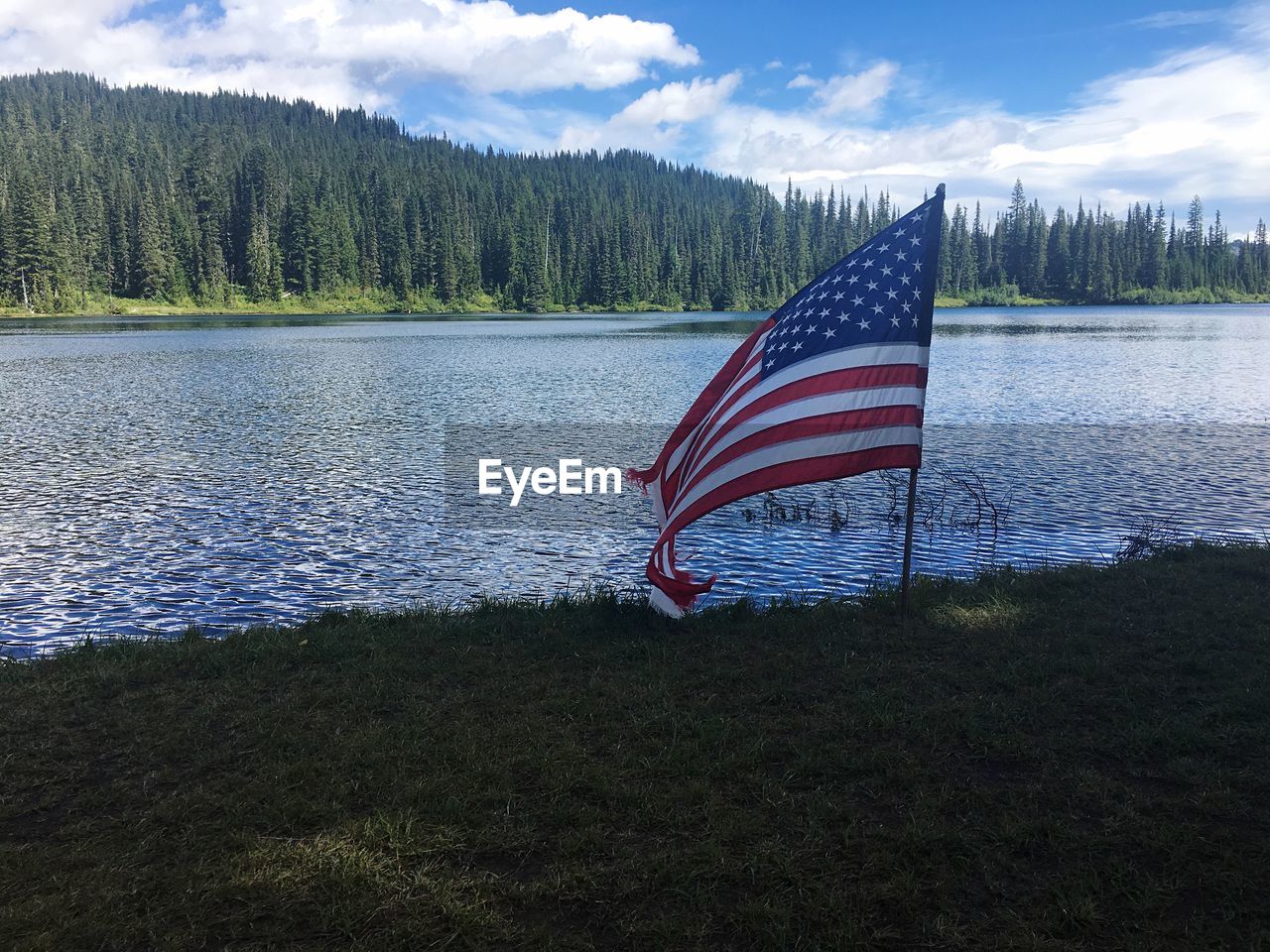 Scenic view of flag by lake against sky