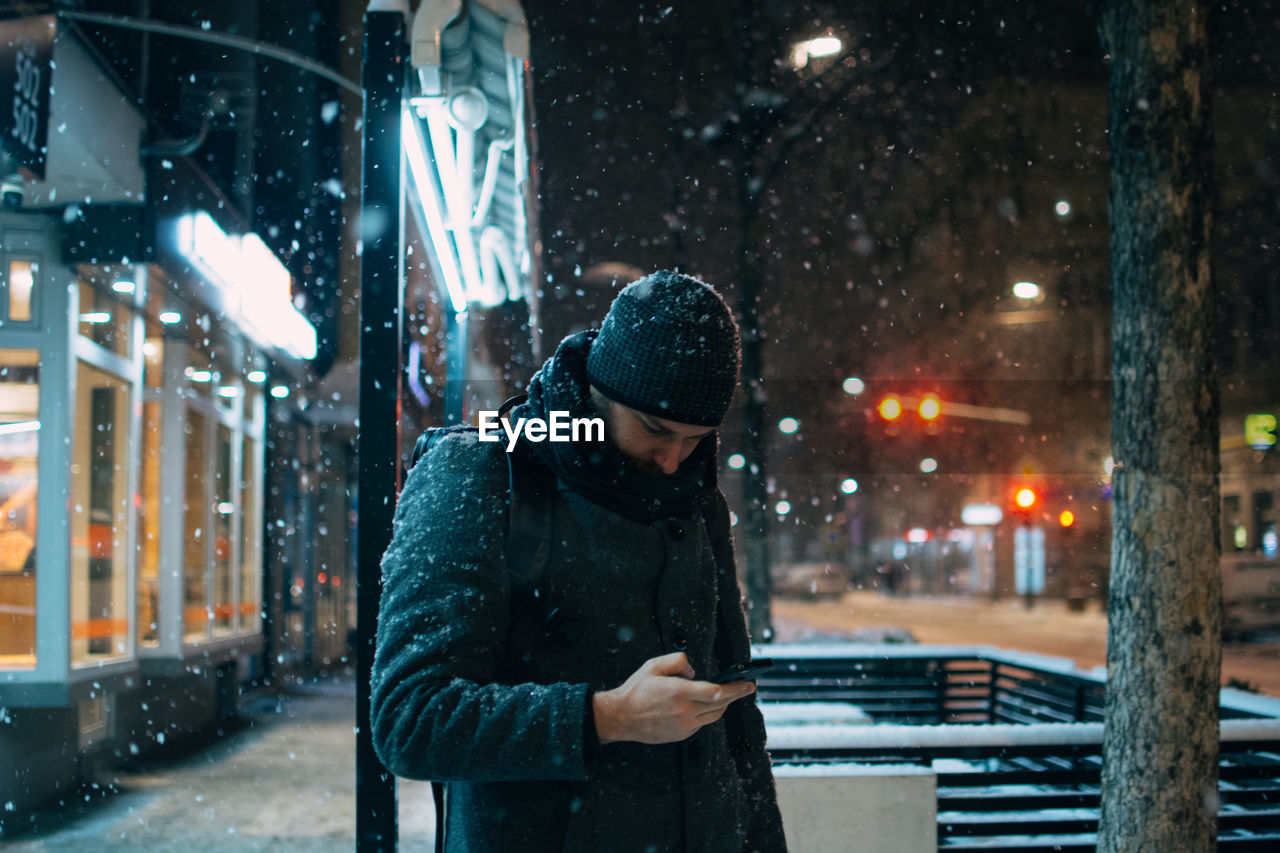 Man using phone on street in city at night during winter