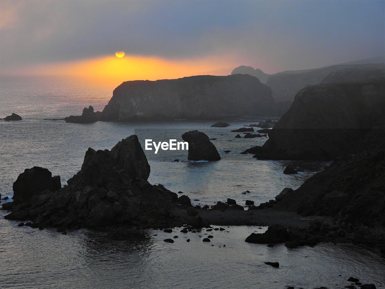 ROCKS ON SEA SHORE AGAINST SUNSET SKY