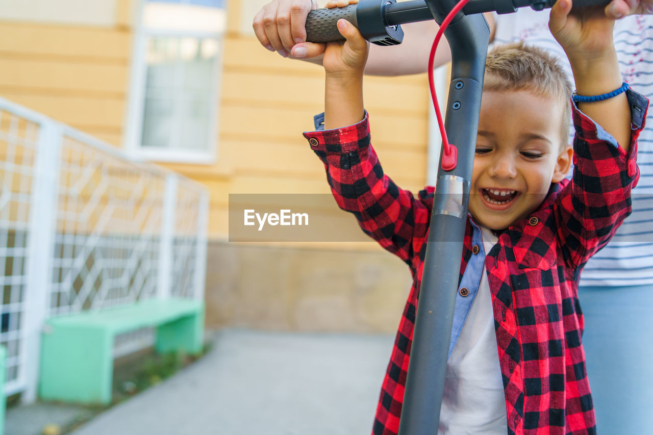 Midsection of mother standing by cheerful son playing with push scooter