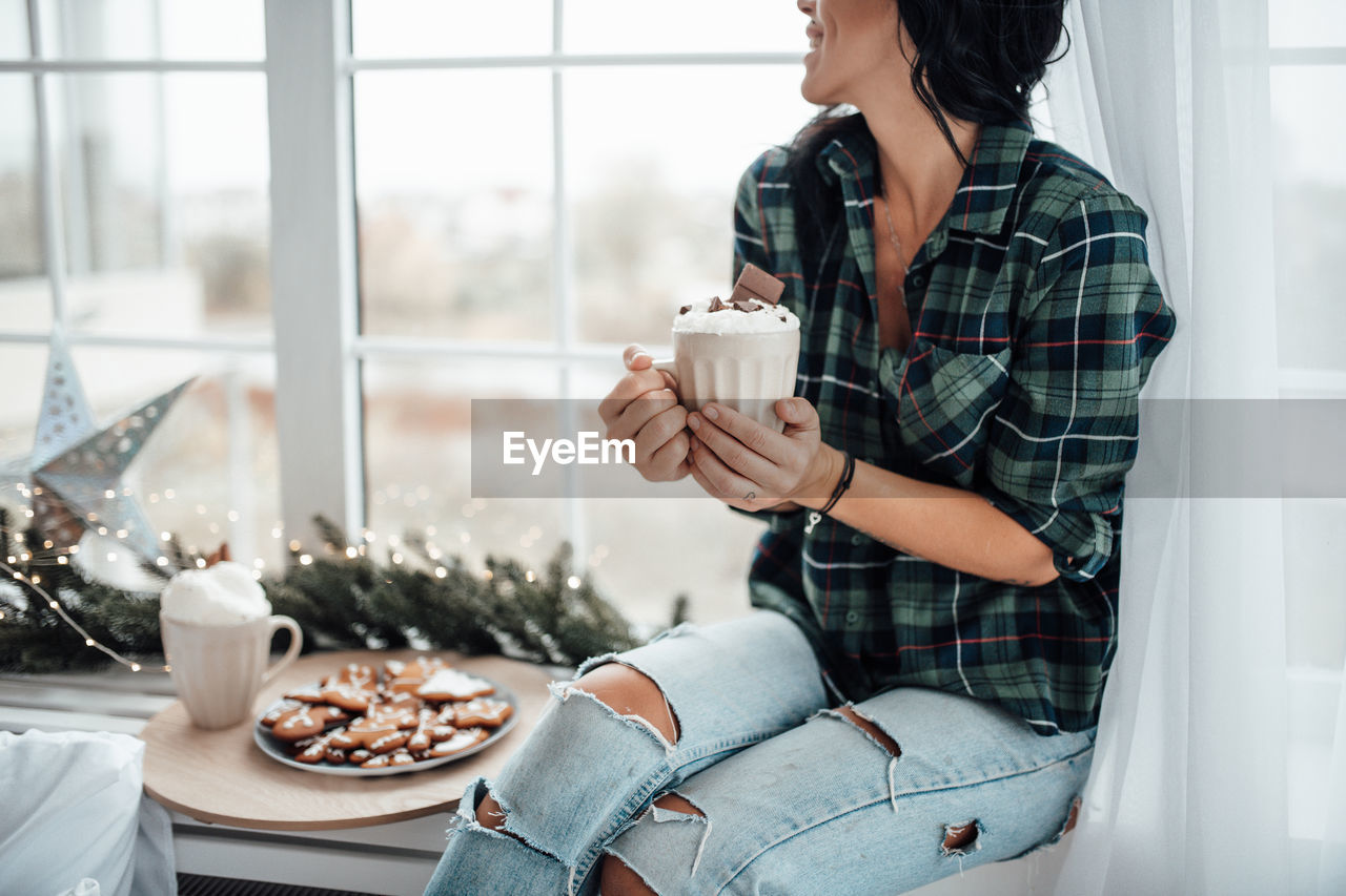 Midsection of woman holding hot chocolate while sitting at home