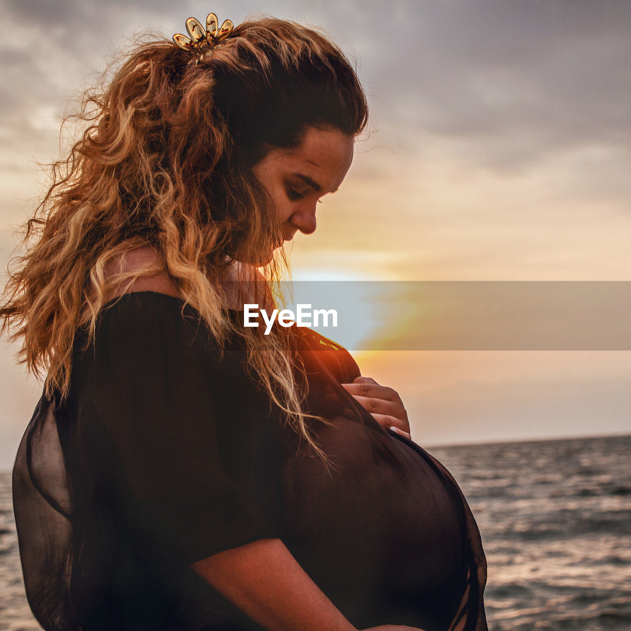 Pregnant woman on beach against sky during sunset
