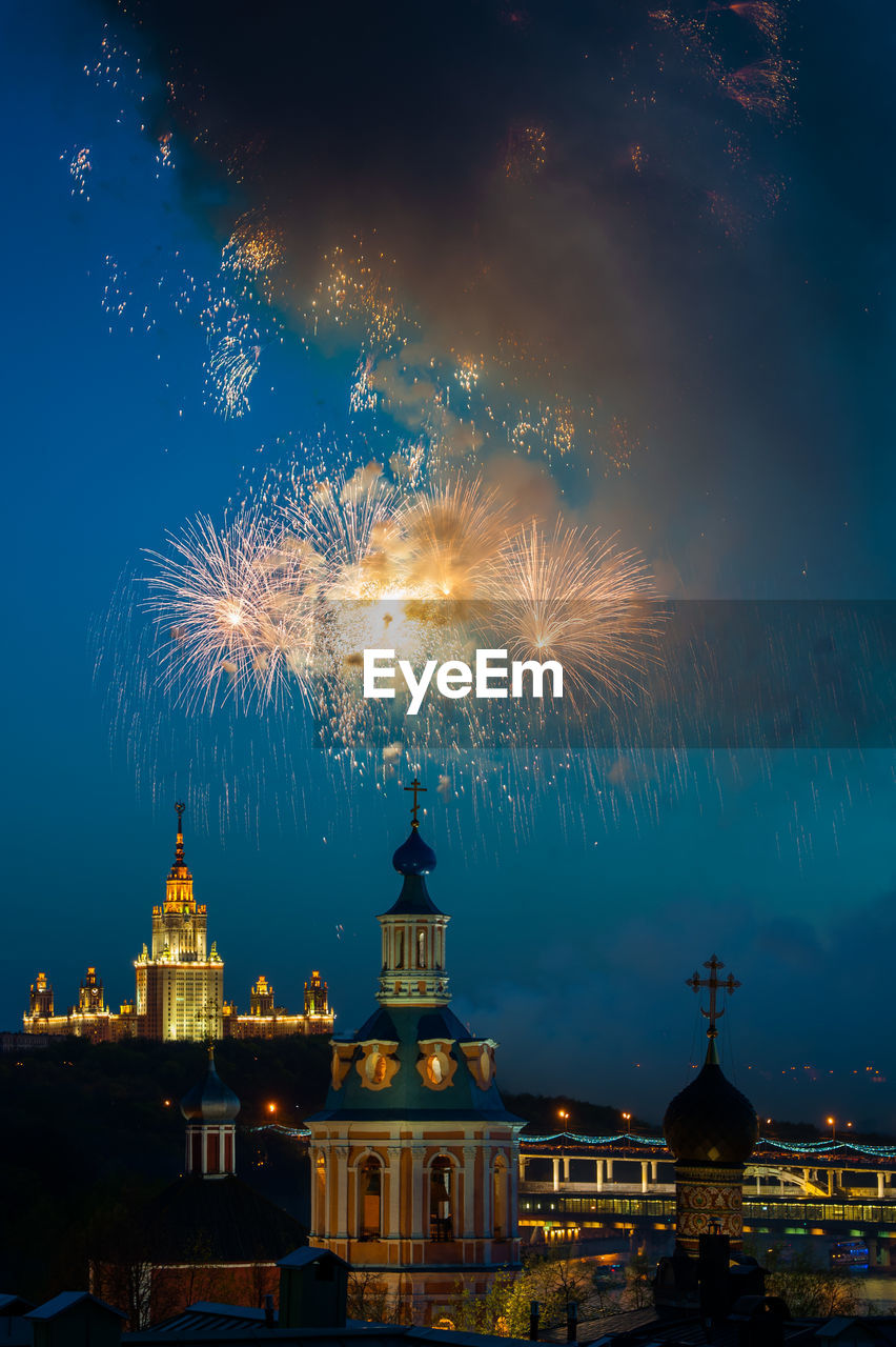 FIREWORK DISPLAY OVER ILLUMINATED BUILDING AGAINST SKY