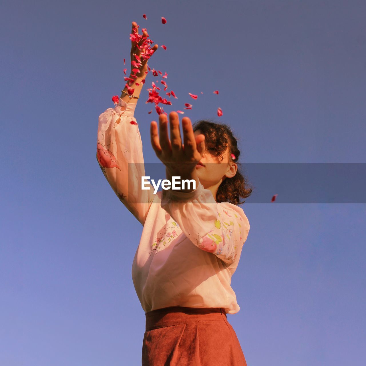 Low angle view of girl holding red against blue sky
