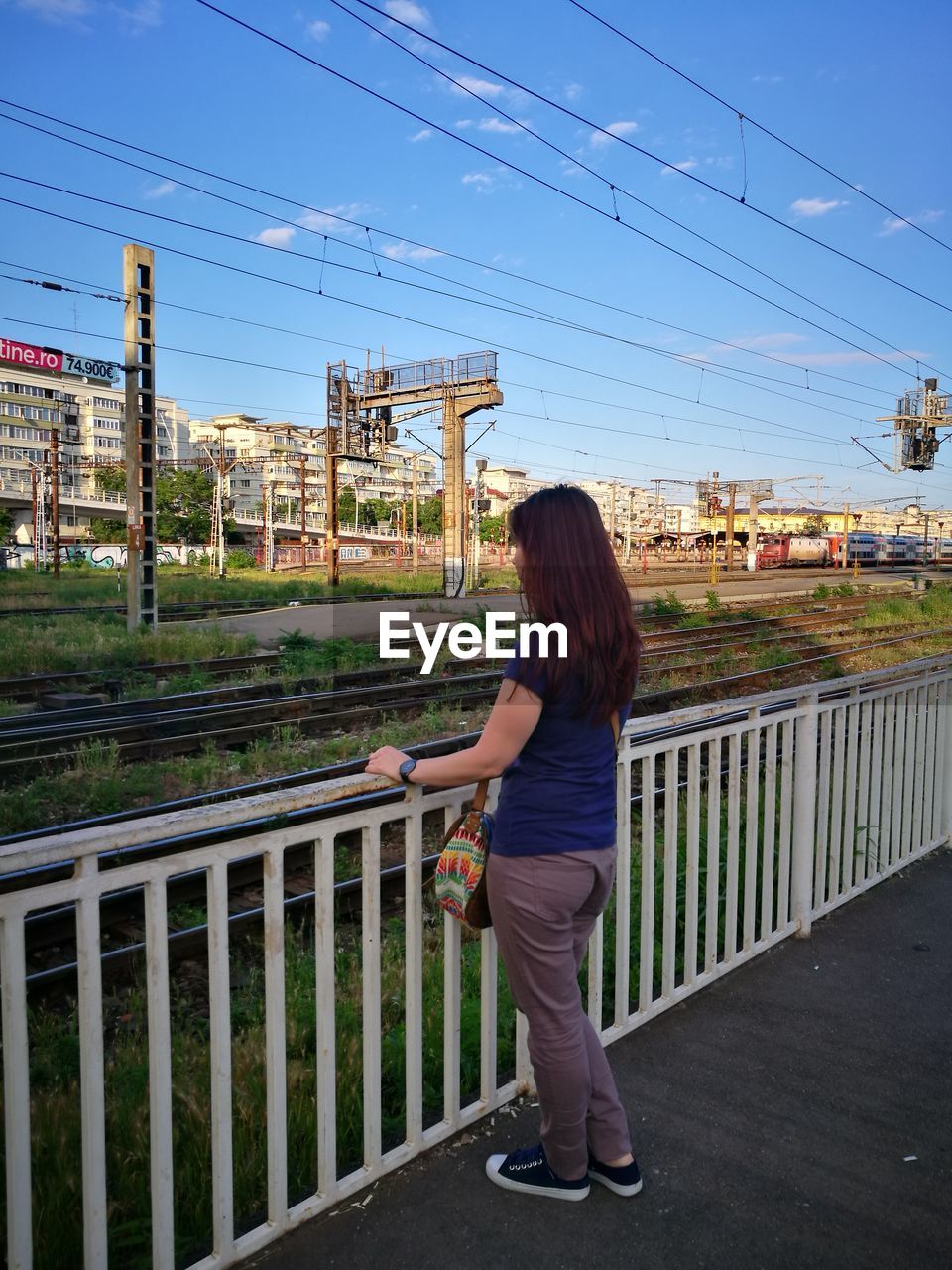 REAR VIEW OF WOMAN STANDING BY RAILING AGAINST SKY