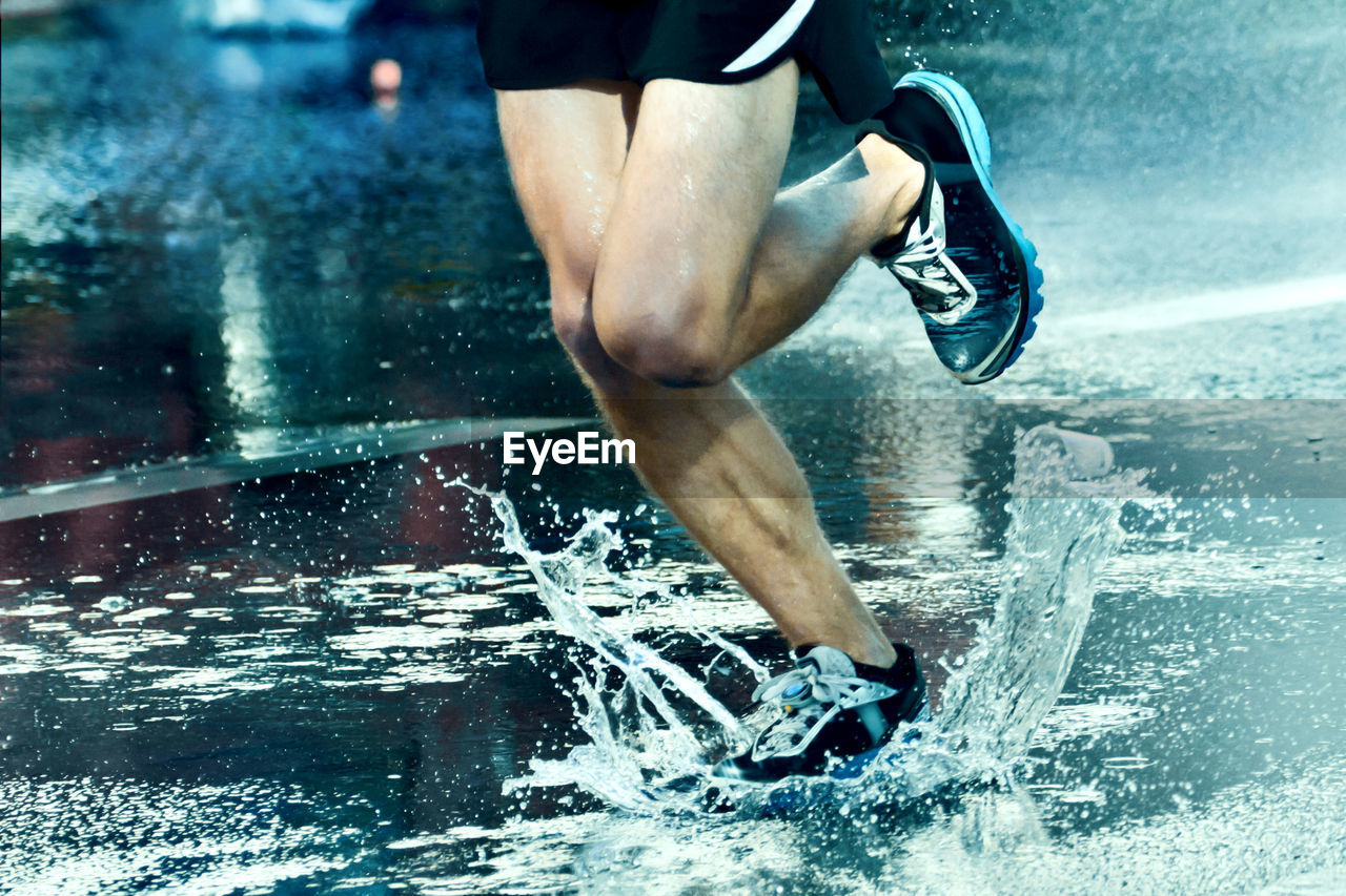 Low section of man running on wet road