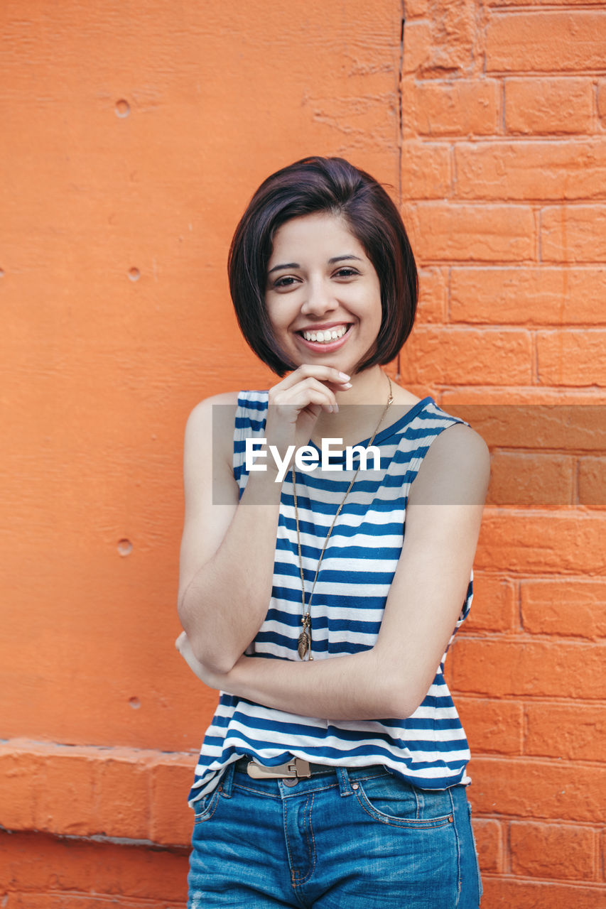 Portrait of smiling young woman standing against wall