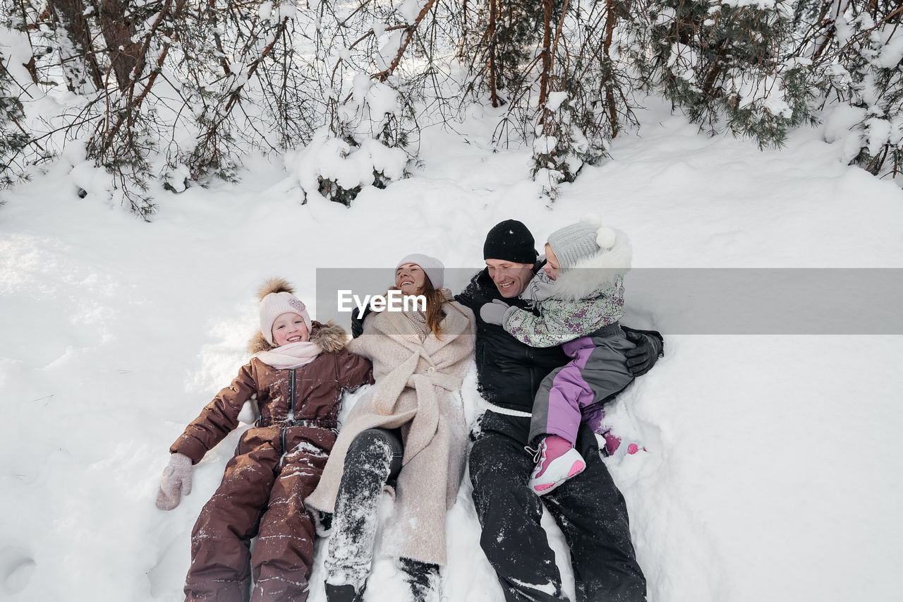 Dad and mom and daughters lying in the snow in the winter forest