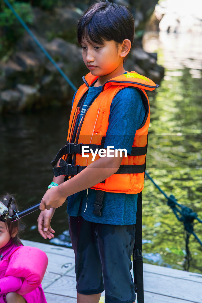  young boy wearing life jacket is feeding fish at the kelah sanctuary in lubuk kejor.