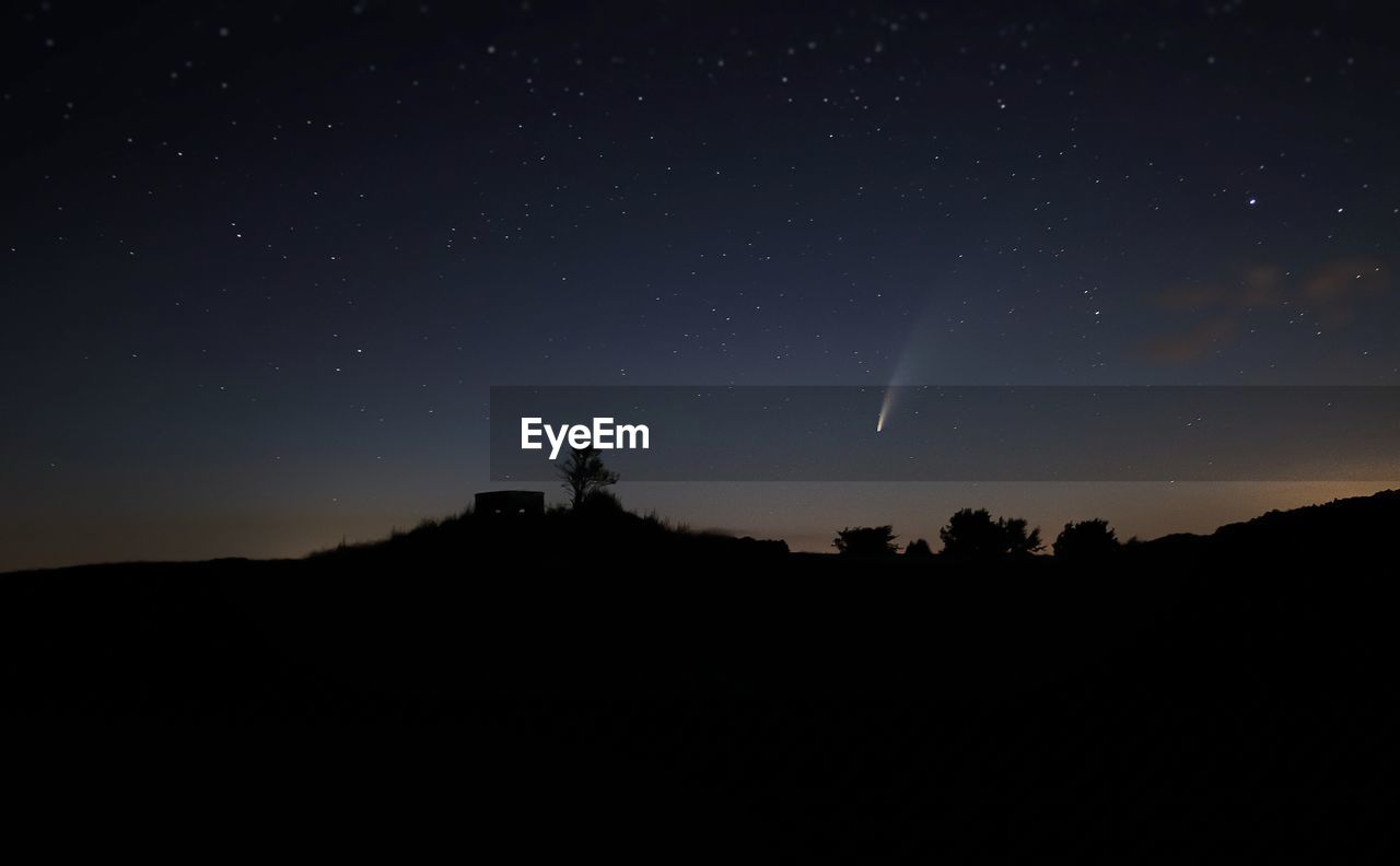 Silhouette landscape against sky at night with meteor