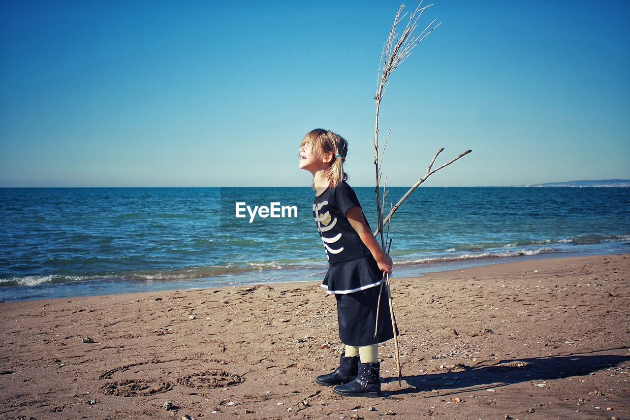 Side view of girl holding branch while standing at beach