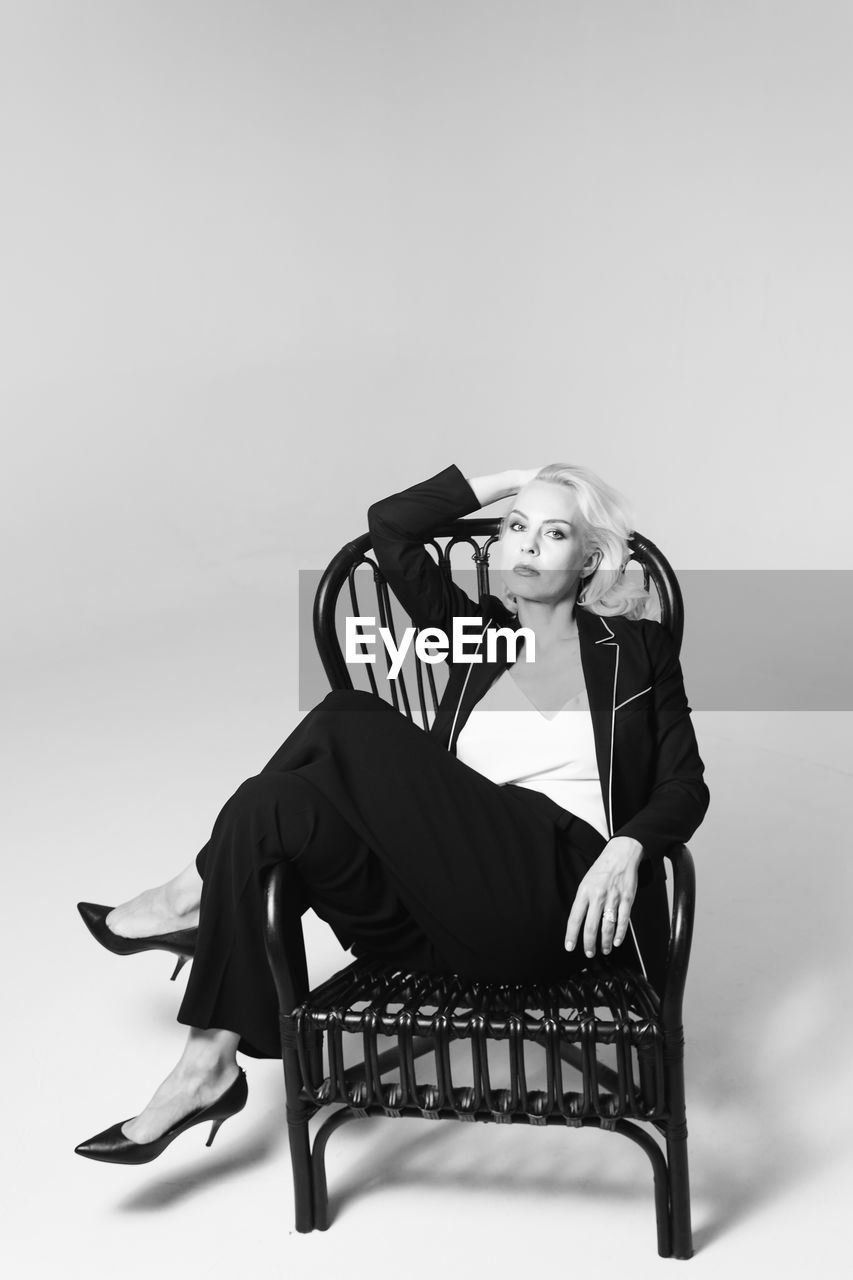 PORTRAIT OF YOUNG WOMAN SITTING ON CHAIR AGAINST CLEAR SKY