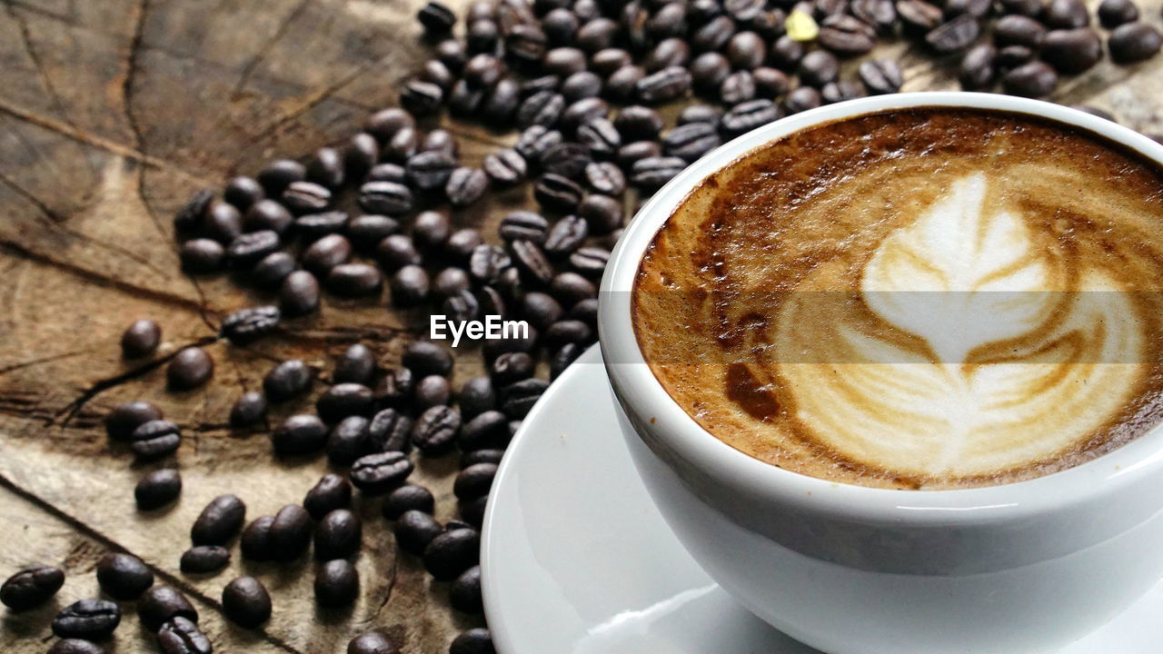 Close-up of cappuccino with roasted coffee beans on table