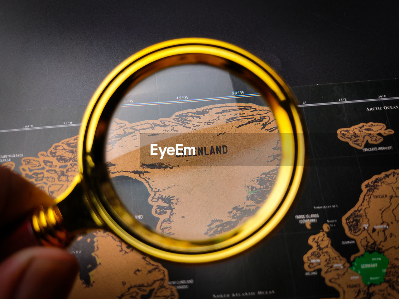 cropped hand holding magnifying glass against black background