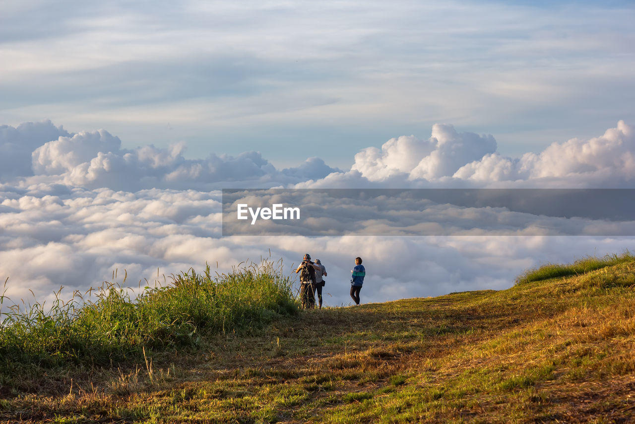 Friends standing on mountain against cloudy sky