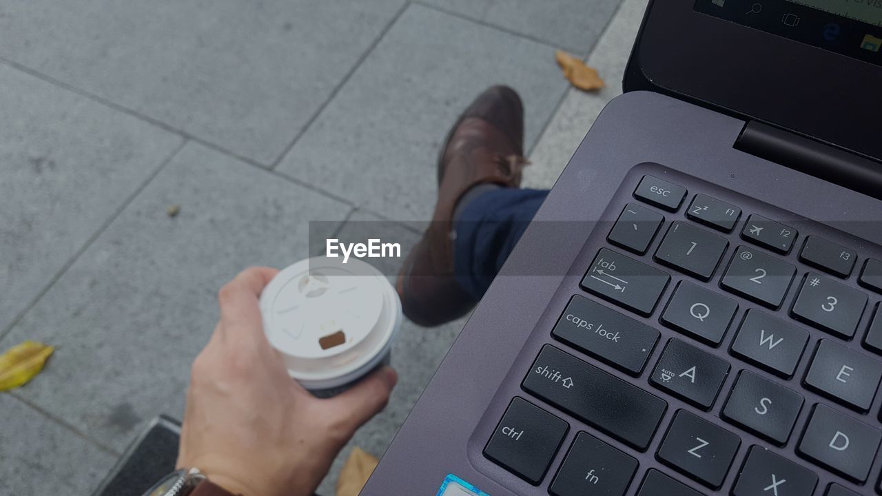 LOW SECTION OF MAN USING SMART PHONE ON LAPTOP