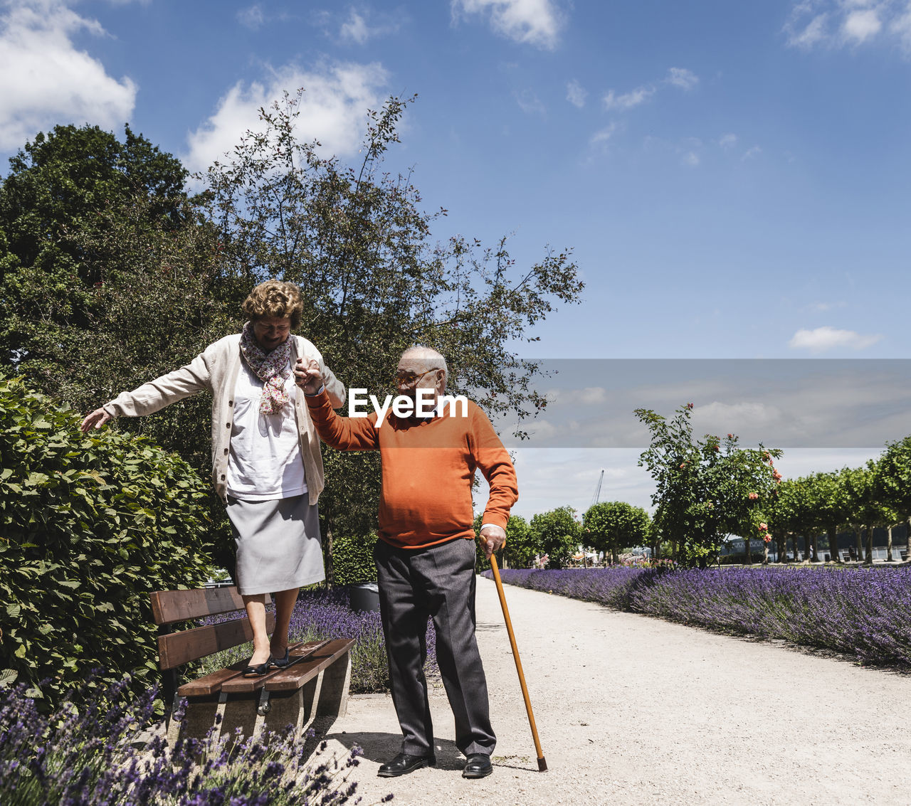 Senior couple having fun in the park, senior man helping womn to balance on bench