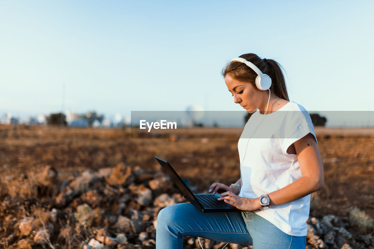 Young woman using laptop on land against sky