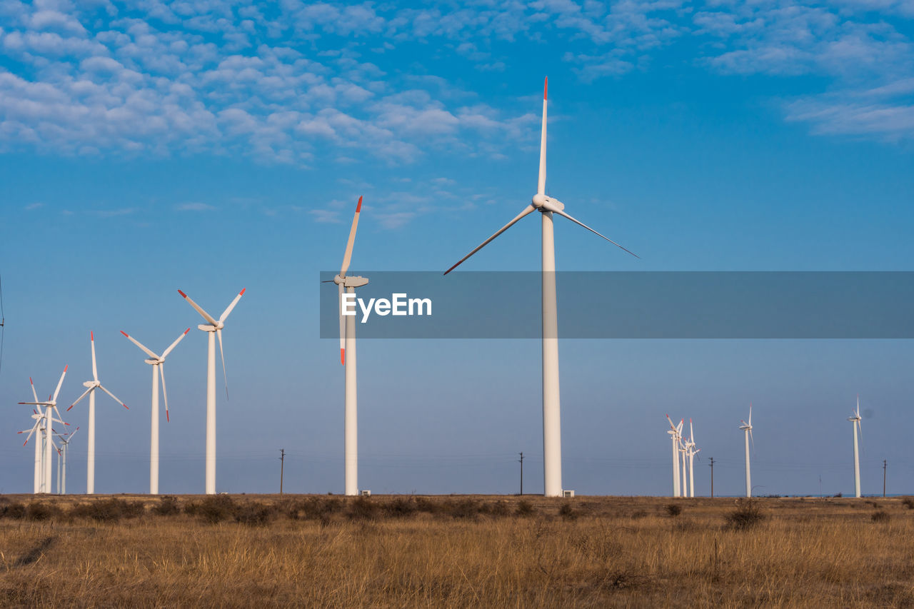 WIND TURBINES ON FIELD AGAINST BLUE SKY