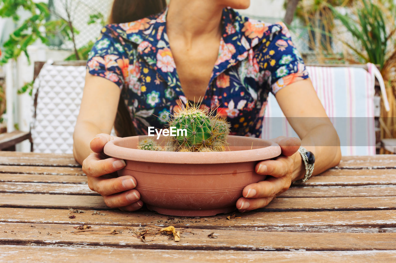 MIDSECTION OF WOMAN HOLDING POTTED PLANT OUTDOORS