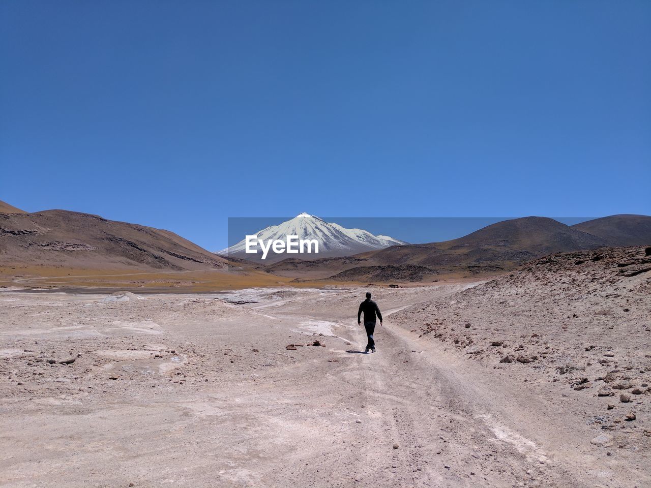 Rear view of man walking on desert against clear blue sky