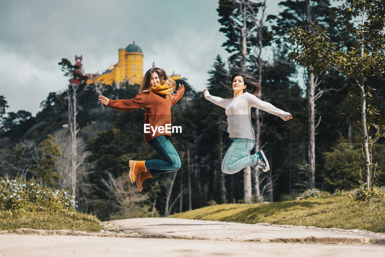 Portrait of beautiful females jumping on street against trees