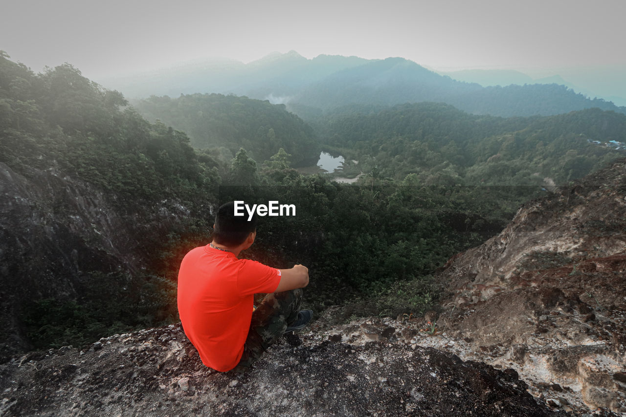 REAR VIEW OF MAN LOOKING AT ROCK