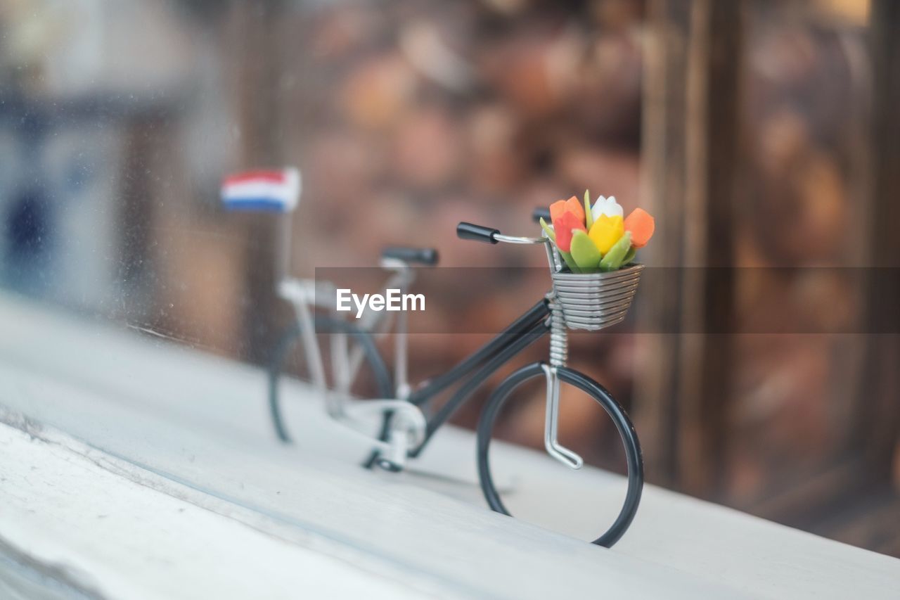 Close-up of toy bicycle on window sill seen through glass