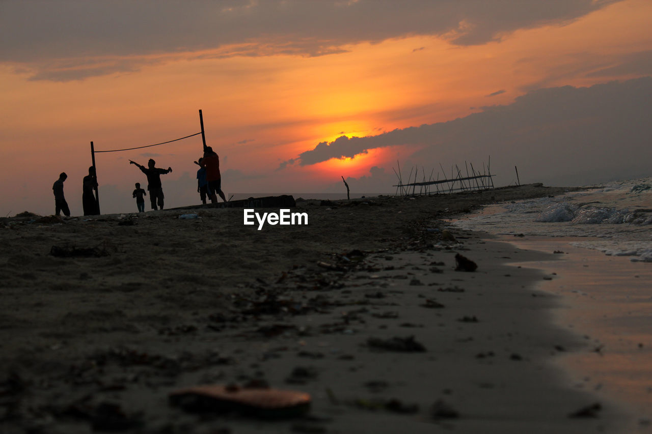 Silhouette people on beach against sky during sunset