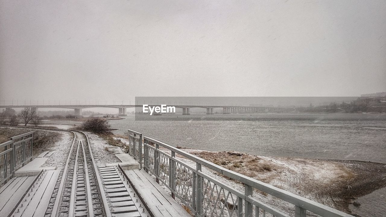 Railroad track by river against clear sky