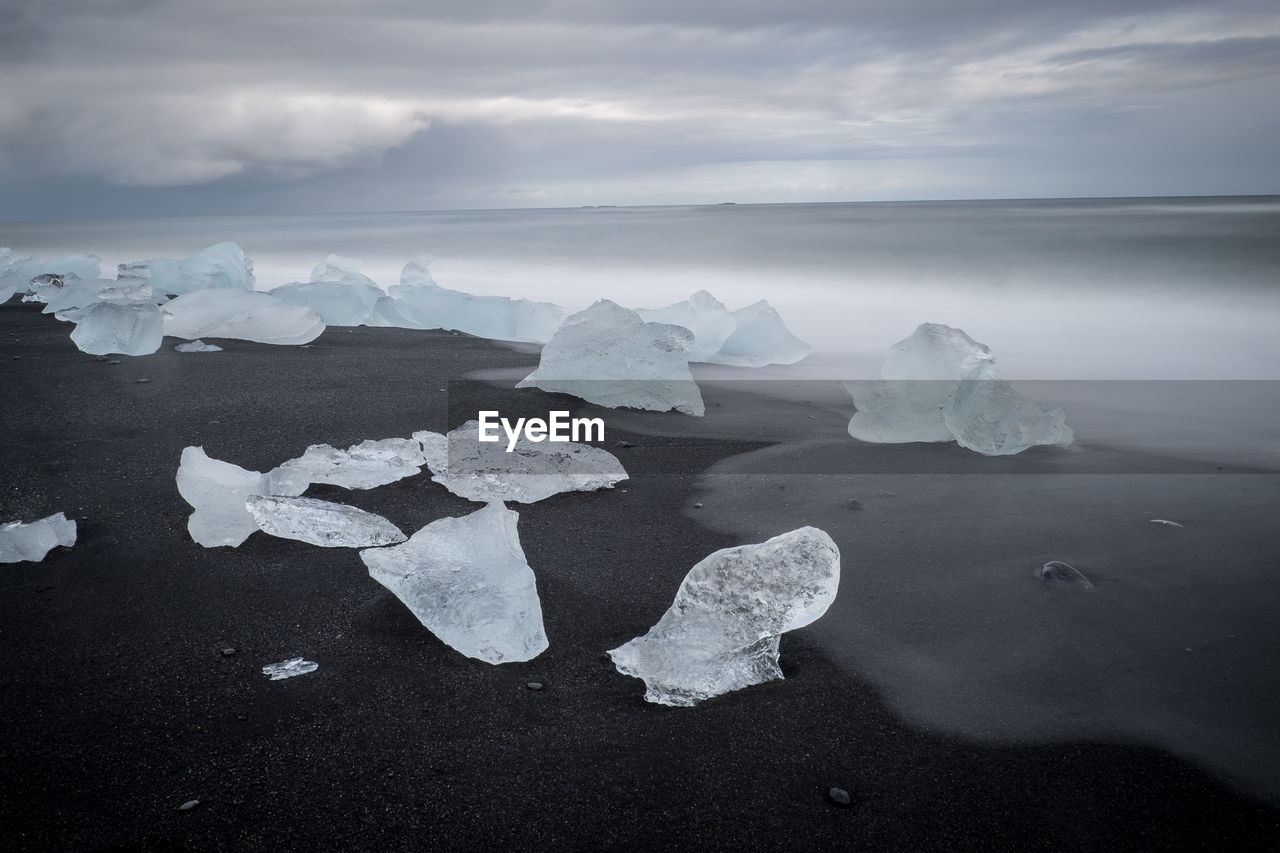 Ice at sea shore against cloudy sky