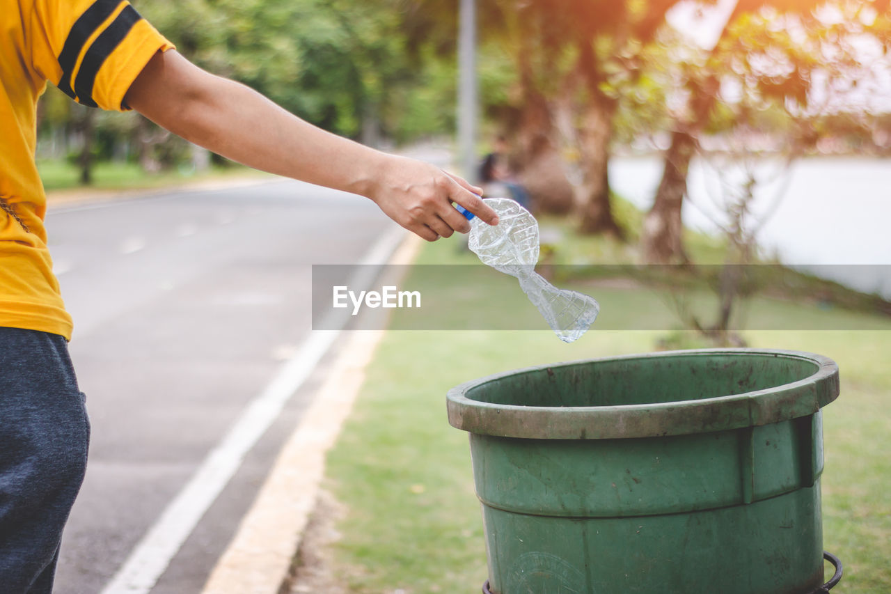 Cropped hand throwing bottle in garbage can