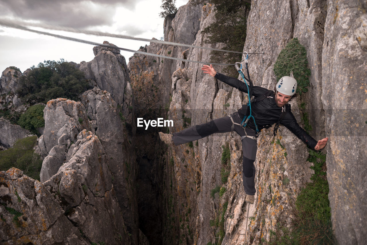 Concept: adventure. climber man with helmet and harness. balancing on the abyss secured on a cable mono bridge. climbing to the top of the mountain. via ferrata on rock.