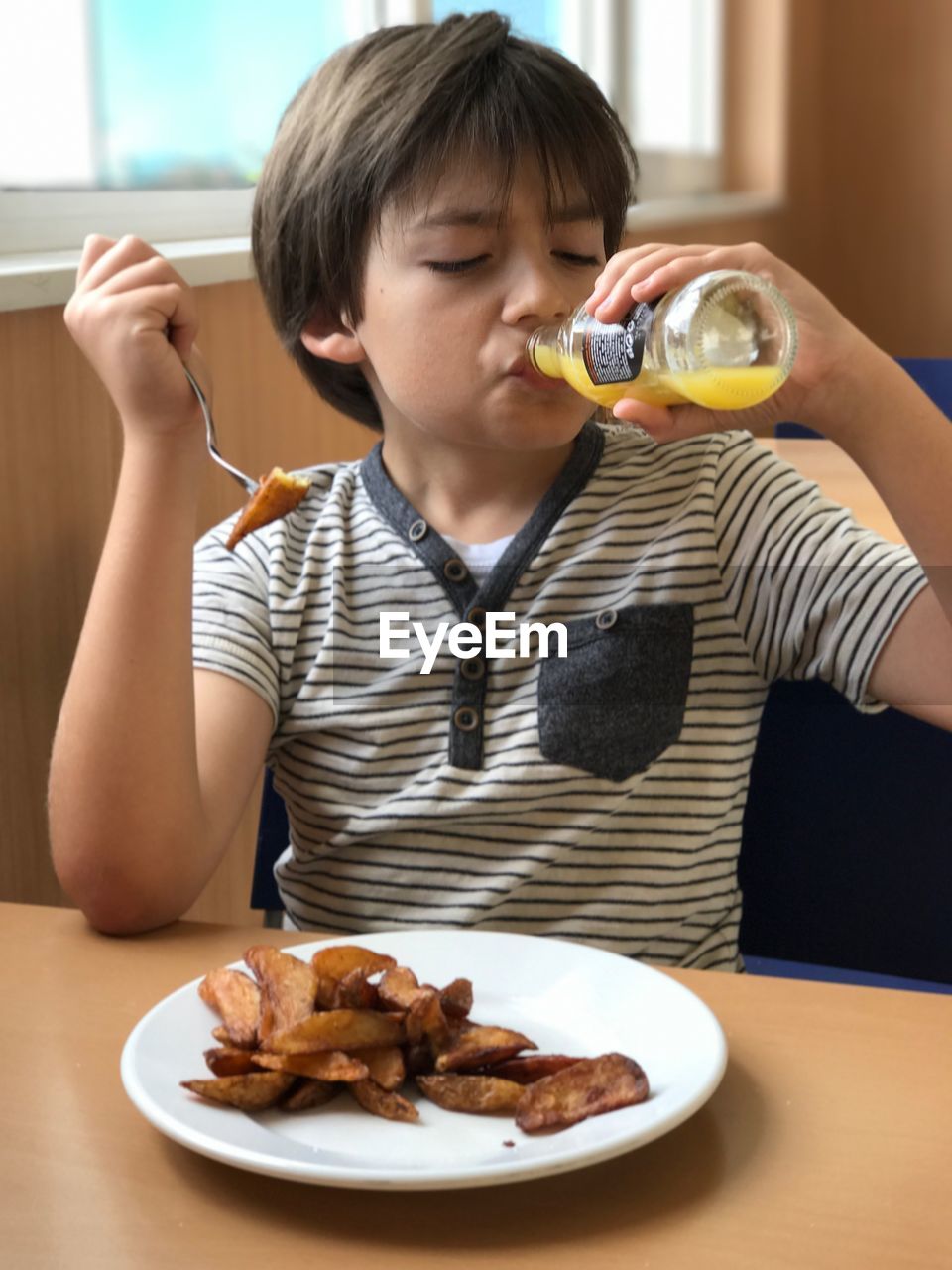 Boy drinking juice from bottle while sitting on chair at restaurant