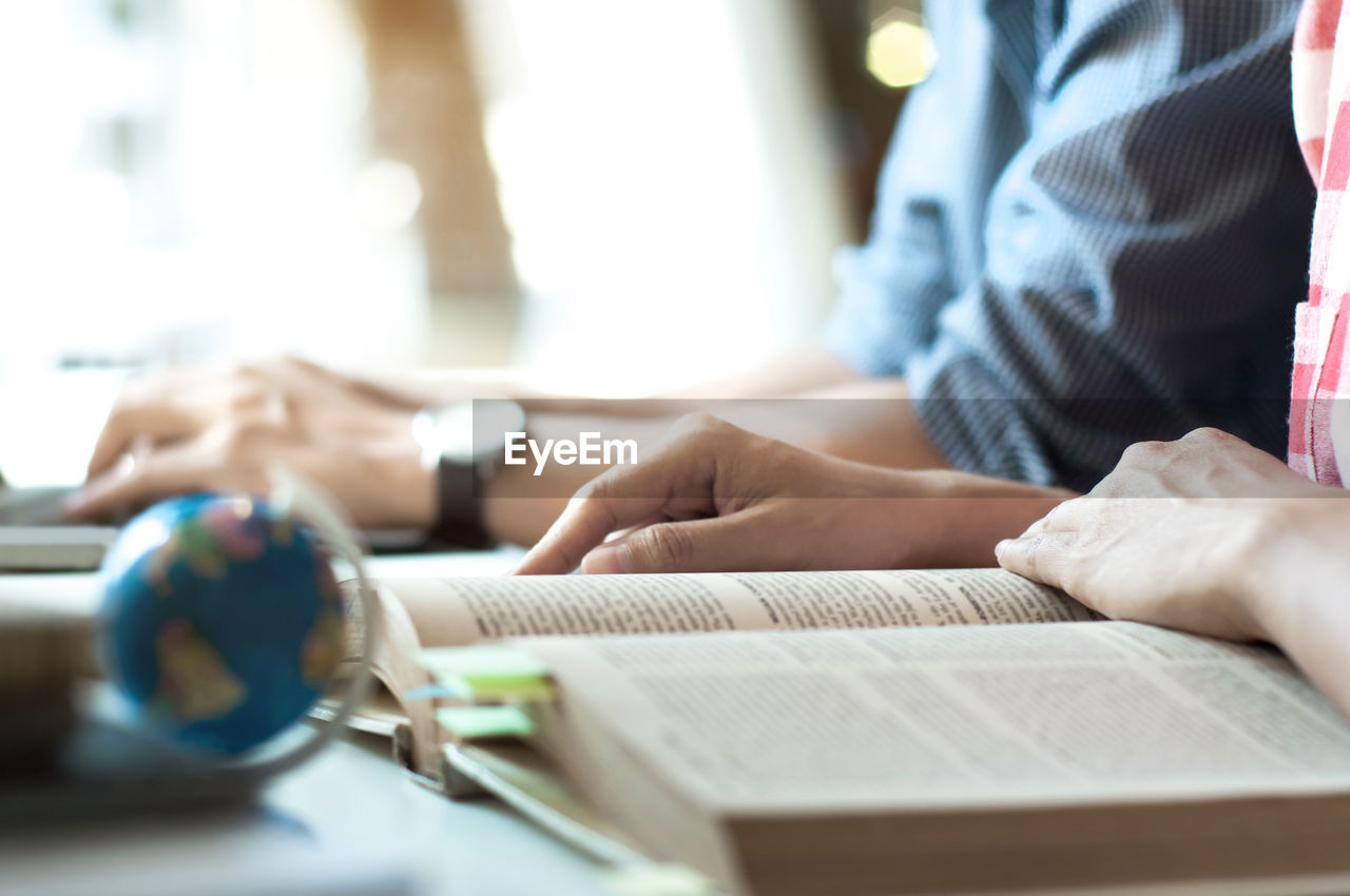 Midsection of woman reading book with male colleague at desk in office