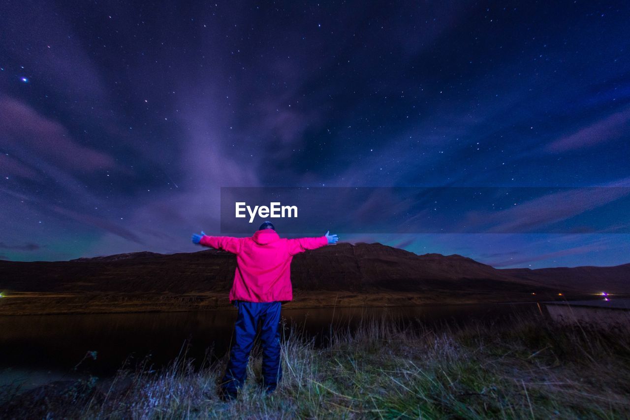 Rear view of man standing on field against sky at night