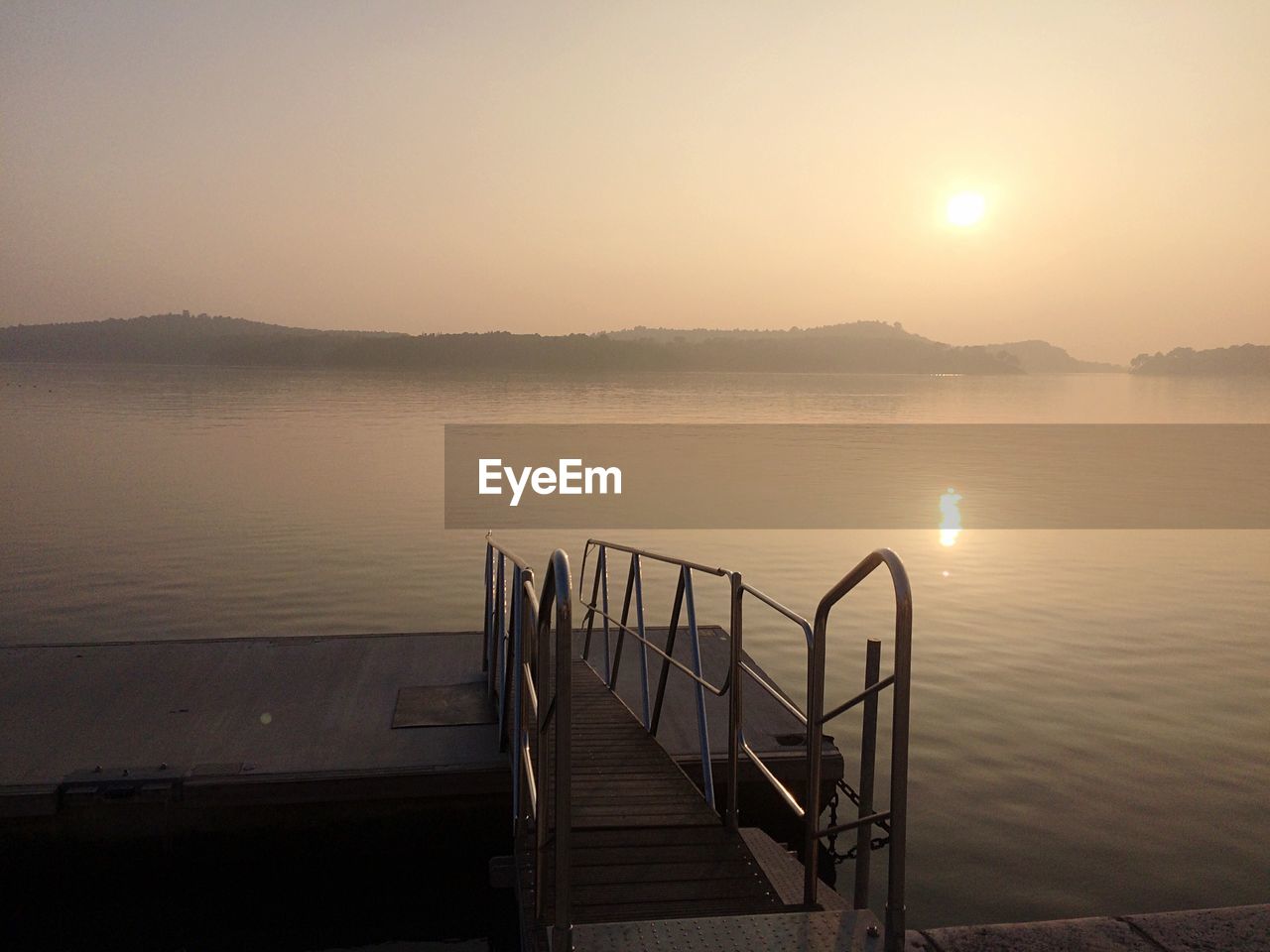 Pier over lake against sky during sunset