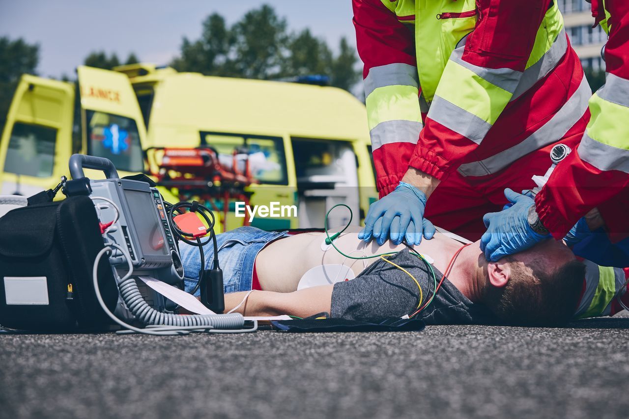 Midsection of paramedic giving cpr to unconscious man lying on street