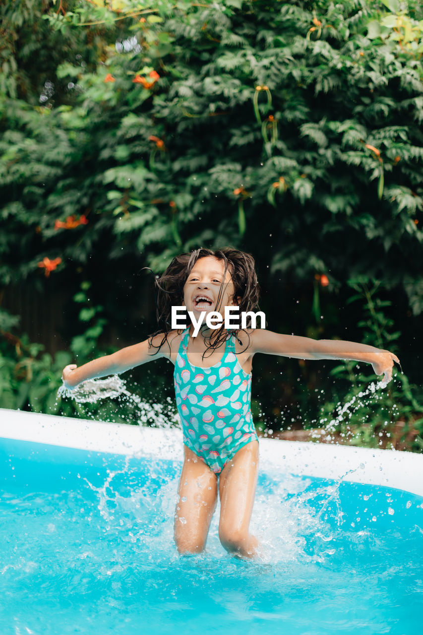 Diverse mixed race toddler girl at home having fun in kiddie pool in backyard being very happy