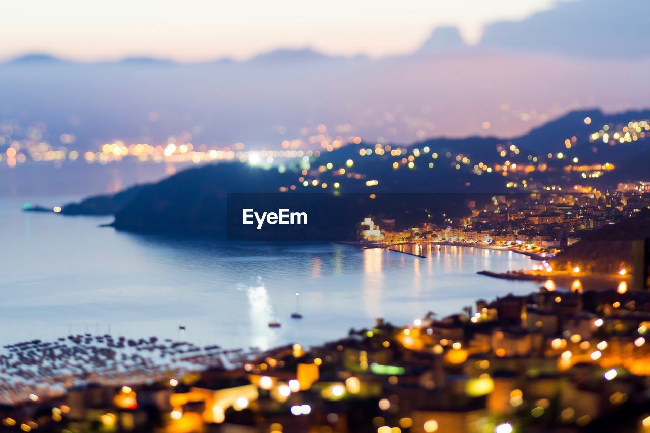 Illuminated cityscape by sea against sky at night