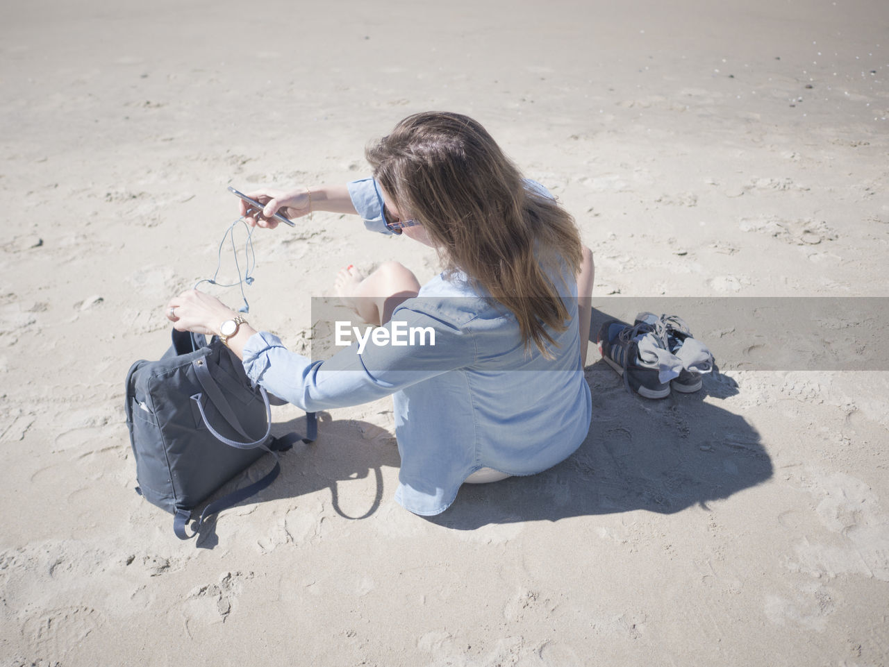 High angle view of woman with mobile phone while taking earphones out of bag at beach