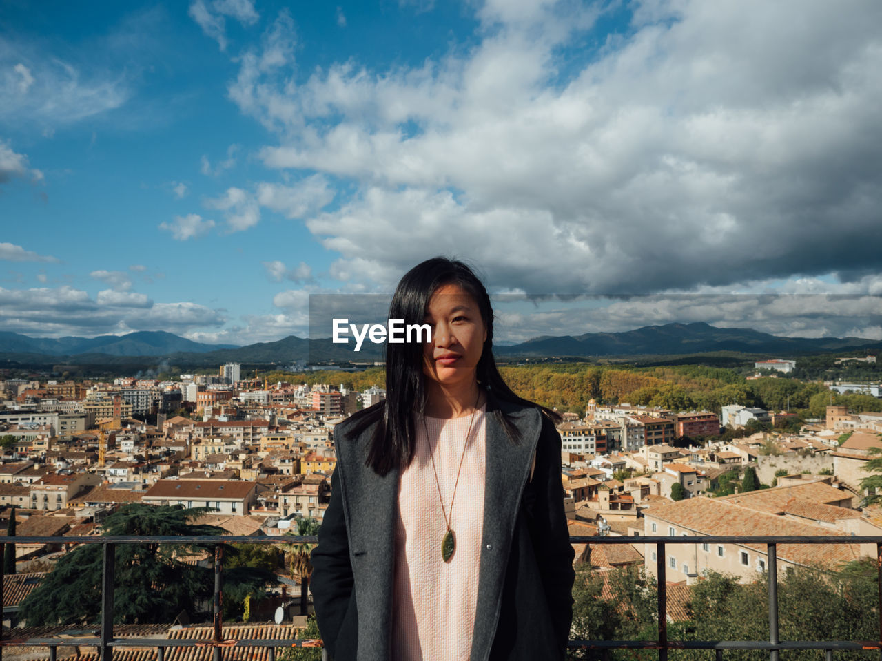 PORTRAIT OF SMILING YOUNG WOMAN STANDING BY BUILDINGS IN CITY