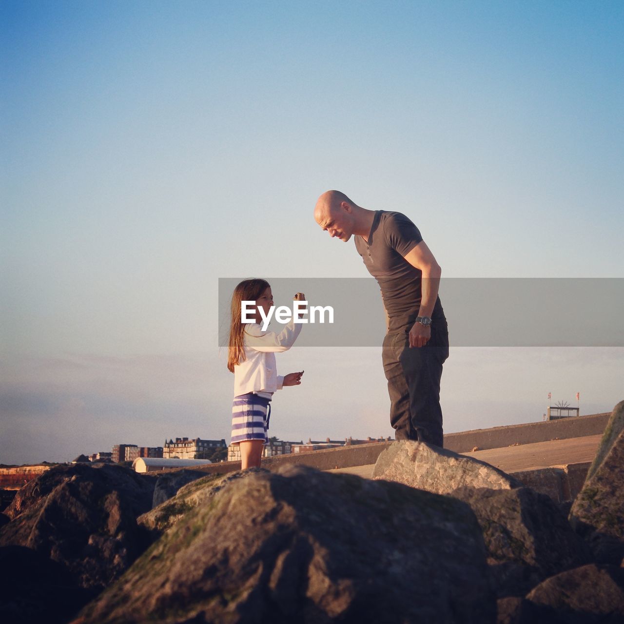 Father with daughter standing on rocks against clear sky