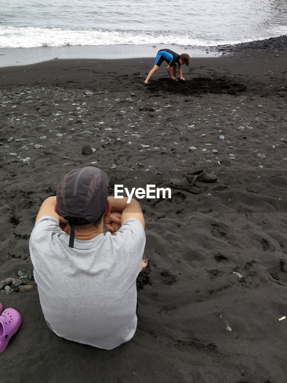 REAR VIEW OF MEN SITTING ON SHORE