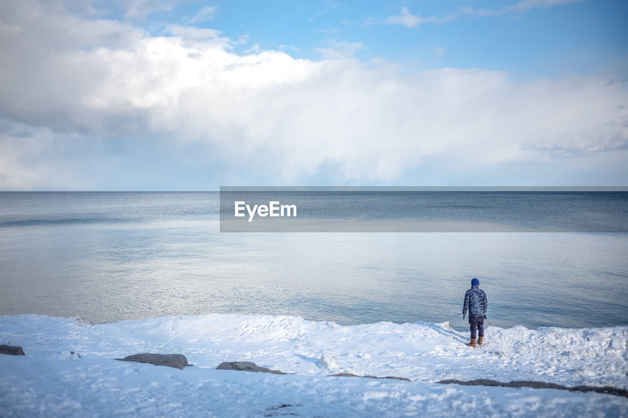 Man on lake against sky during winter