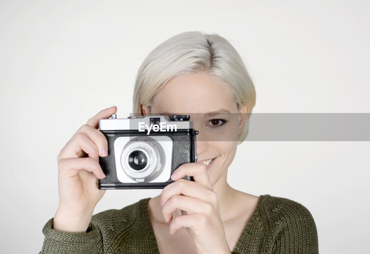 Close-up portrait of young woman photographing while standing against white background