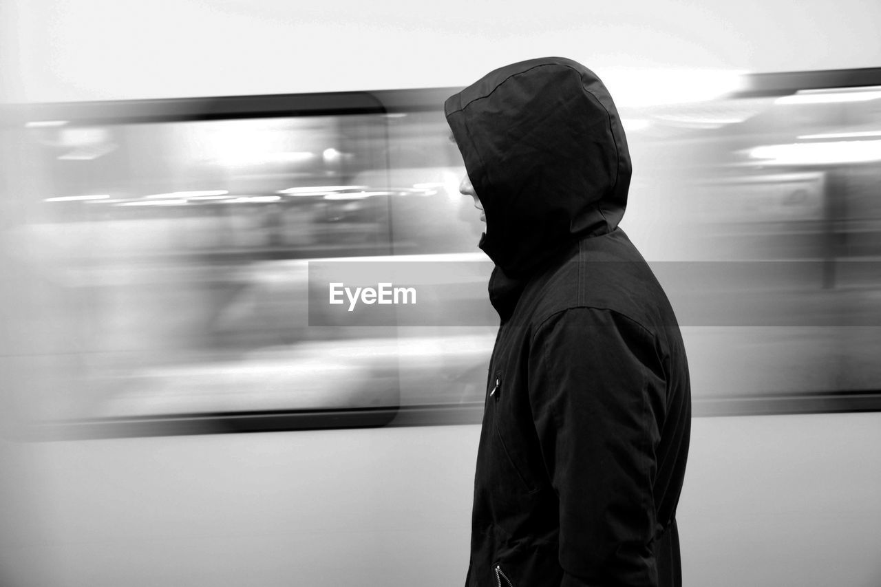 Side view of person in hooded shirt standing by moving train at